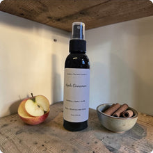 Load image into Gallery viewer, Bottle of Apple Cinnamon-scented spray on a wooden surface with apples and cinnamon sticks.