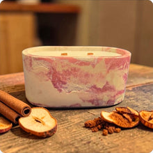 Load image into Gallery viewer, Marbled pink and white candle on a wooden surface with cinnamon sticks, apples, and nuts.