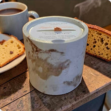 Load image into Gallery viewer, Candle in a rustic container with a cup of coffee and banana nut bread slices on a wooden surface