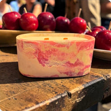 Load image into Gallery viewer, Marbled pink candle on a wooden surface with red candy apples in the background
