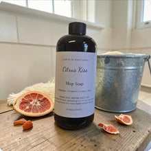 Load image into Gallery viewer, Bottle of Citrus Kiss Mop Soap on a wooden surface with a bucket and grapefruit slices in the background.