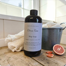 Load image into Gallery viewer, Bottle of Citrus Kiss Mop Soap on a wooden surface with a bucket and grapefruit slices in the background.