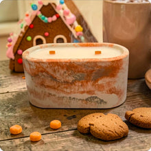 Load image into Gallery viewer, Candle in a decorative concrete container with gingerbread house and cookies on a wooden surface