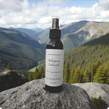 Load image into Gallery viewer, Bottle of 'Mahogany Teakwood' on a rock with a mountainous landscape in the background