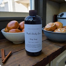 Load image into Gallery viewer, Bottle of Maple Sticky Bun Mop Soap on a wooden surface with cinnamon sticks and bowls of buns in the background.