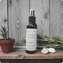 Load image into Gallery viewer, Spray bottle labeled 'Sea Salt & Rosemary' on a wooden surface with rosemary plants and stones.