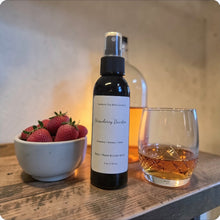 Load image into Gallery viewer, Bottle of Strawberry Bourbon-scented spray next to a glass of bourbon and bowl of strawberries on a wooden surface.
