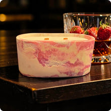 Load image into Gallery viewer, Candle in a decorative concrete container on a wooden surface with a glass of bourbon and strawberries.