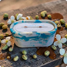 Load image into Gallery viewer, Candle with a marbled design on a wood surface with pistachio nuts, caramel and jasmine flowers
