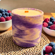 Load image into Gallery viewer, Concrete candle with purple marbled design on a woven mat with bowls of berries in the background.
