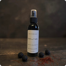 Load image into Gallery viewer, Black spray bottle with a label "Blackberry &amp; Saffron" on a dark surface with blackberries and saffron.

