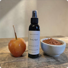 Load image into Gallery viewer, Bottle of 'Candy Apple' spray next to a caramel candy apple and a bowl of brown sugar on a wooden surface.
