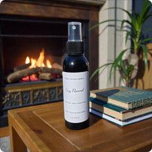 Load image into Gallery viewer, Black spray bottle labeled 'Cozy Flannel' on a wooden table with a fireplace and books in the background
