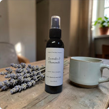 Load image into Gallery viewer, Bottle of Lavender &amp; Chamomile room spray on a wooden table with lavender and a mug.
