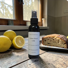 Load image into Gallery viewer, Lemon Pound Cake-scented spray bottle on a wooden surface with lemons and a lemon pound cake in the background.
