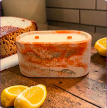 Load image into Gallery viewer, Concrete marbled candle on a wooden surface with lemons and lemon pound cake in background.
