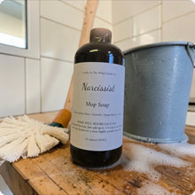 Load image into Gallery viewer, Bottle of 'Narcissist' Mop Soap on a wooden surface with cleaning tools in the background.
