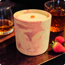 Load image into Gallery viewer, Candle in a decorative concrete container on a wooden surface with a glass of bourbon and strawberries.
