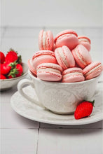 Load image into Gallery viewer, Pink macarons in a white teacup with strawberries on a light wooden surface
