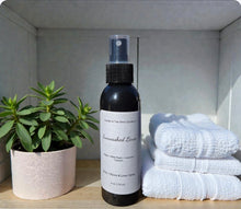 Load image into Gallery viewer, Black spray bottle with Sunwashed Linen Body/ Room &amp; Linen Spray, white towels, and a plant on a wooden surface.

