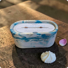 Load image into Gallery viewer, Marbled blue and white concrete candle on a wooden surface with a dollop of whipped cream.
